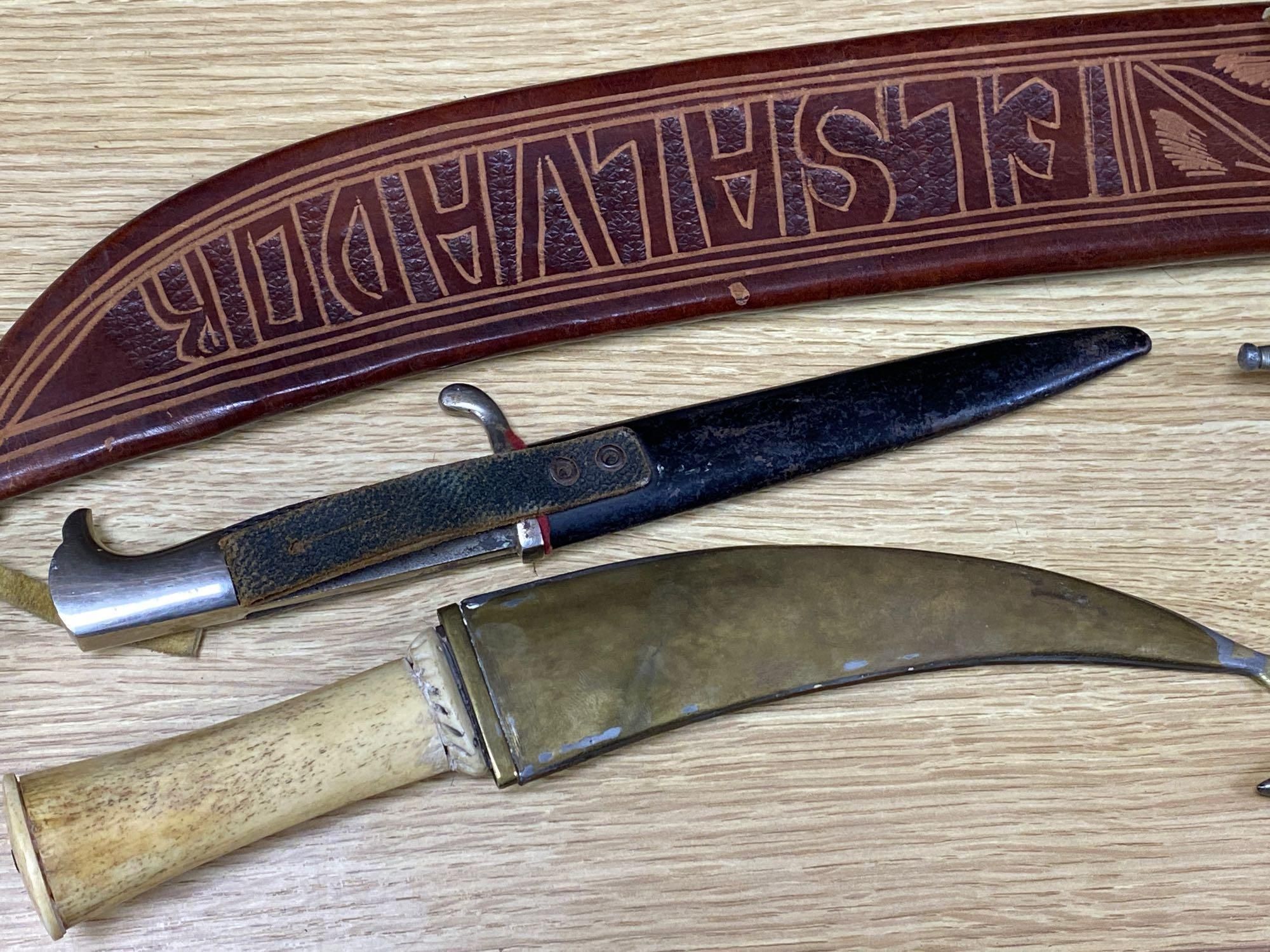 Five various weapons including a Kukri, a carved bone handled dagger with brass sun, moon and stars sheath and an El Salvador machete